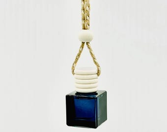 May include: A small, square, dark blue glass bottle with a wooden cap and a braided tan rope for hanging. The bottle is filled with a dark liquid. The wooden cap has a series of white, circular layers. The rope is attached to a white, spherical bead.