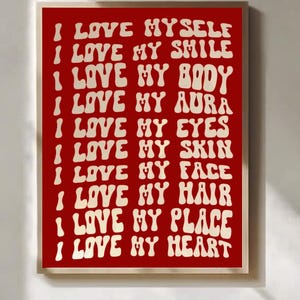 May include: A framed print with a red background and white text. The text reads "I LOVE MYSELF, I LOVE MY SMILE, I LOVE MY BODY, I LOVE MY AURA, I LOVE MY EYES, I LOVE MY SKIN, I LOVE MY FACE, I LOVE MY HAIR, I LOVE MY PLACE, I LOVE MY HEART."
