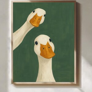 Könnte beinhalten: Ein gerahmter Kunstdruck mit zwei weißen Gänsen mit orangefarbenen Schnäbeln und schwarzen Augen vor einem dunkelgrünen Hintergrund. Die Gänse sind in einem skurrilen Stil gemalt, wobei eine teilweise von der Seite sichtbar ist.