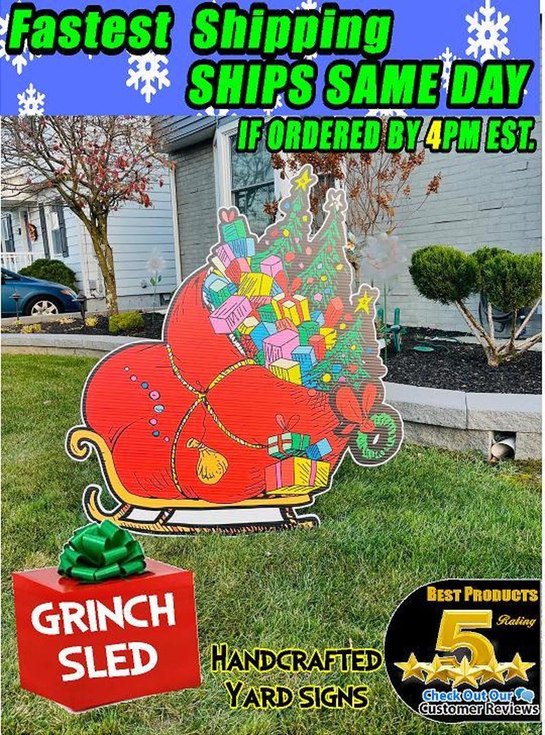 May include: A red Grinch sleigh filled with colourful presents and a Christmas tree. The sleigh is on a green lawn in front of a house. The text "GRINCH SLED" is on a red box in the foreground. The text "HANDCRAFTED YARD SIGNS" is on the bottom of the image.