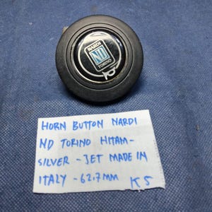 Könnte beinhalten: Schwarzer Nardi-Hupenknopf mit silbernem und weißem Logo. Der Text "NARDI TORINO" ist sichtbar. Der Knopf hat einen Durchmesser von 6,27 cm. Der Text "HORN BUTTON NARDI ND TORINO HITAM - SILVER - JET MADE IN ITALY" ist ebenfalls sichtbar.
