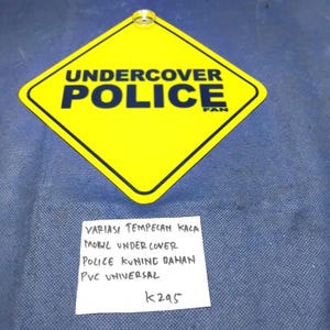 May include: A yellow diamond-shaped sign with the words "UNDERCOVER POLICE FAN" in black. The sign has a metal ring at the top. A handwritten note below the sign includes text in a foreign language and the number "k295".