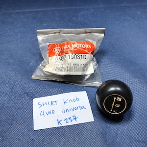 May include: A black shift knob with a circular design indicating 2H, 4H, and 4L settings. The image also shows a Kia Motors parts package and a handwritten note that reads "SHIRT Knob 4WD Universal K 237".