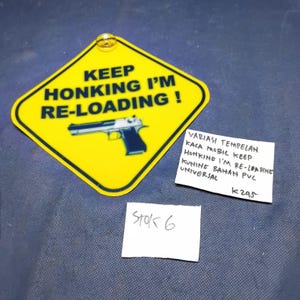 May include: A yellow diamond-shaped sticker with black text that reads "KEEP HONKING I'M RE-LOADING!". A silver and black handgun graphic is below the text. A small white note reads "STOK 6".