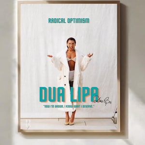 Può includere: Un poster incorniciato con la scritta "RADICAL OPTIMISM" in turchese. Il nome "DUA LIPA" è in turchese e arancione. L'immagine mostra una persona in abito bianco e la citazione "NOW I'M GROWN, I KNOW WHAT I DESERVE."