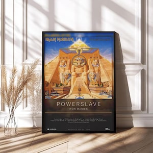 Könnte beinhalten: Gerahmtes Poster mit dem Albumcover von Iron Maidens "Powerslave". Das Kunstwerk zeigt eine ägyptisch inspirierte Szene mit Pyramide und Statuen. Das Poster, in einem schwarzen Rahmen, wird in Innenräumen präsentiert.
