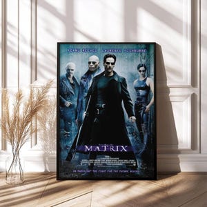 May include: Framed movie poster for "The Matrix" featuring Keanu Reeves, Laurence Fishburne, and others. The poster has a black frame and displays the film's title in large, stylized letters. The background is a mix of blue and black.