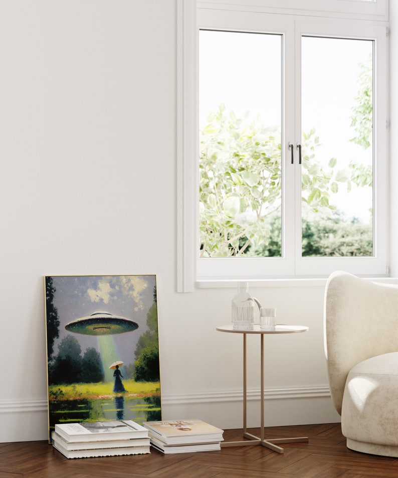 Op de afbeelding: Een ingelijst schilderij van een vrouw die in een veld staat met een vliegende schotel die boven haar zweeft. Het schilderij staat op een plank met een stapel boeken eronder. Een kleine ronde tafel met een glazen vaas en een glas water staat voor het schilderij.