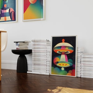 Puede incluir: Una impresi&oacute;n enmarcada de una ilustraci&oacute;n abstracta colorida de un platillo volante con un orbe brillante en el fondo. La impresi&oacute;n se apoya en una pila de revistas.