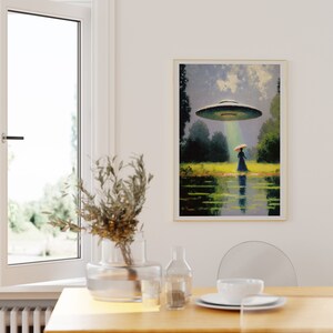 Op de afbeelding: Een ingelijst schilderij van een vrouw die over een veld loopt met een UFO die boven haar zweeft. De vrouw draagt een lange jurk en een hoed. De UFO straalt een lichtstraal naar beneden op haar. Het schilderij is geschilderd tegen een achtergrond van een blauwe lucht met witte wolken.