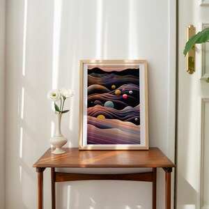 May include: A framed abstract art print with a dark background and colourful orbs. The print features a landscape of swirling, layered lines in shades of purple, blue, and brown. The frame is a light wood colour.