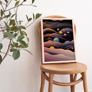 May include: A framed abstract art print with a dark background and colourful planets and stars. The print is in a light wood frame and is sitting on a wooden chair.
