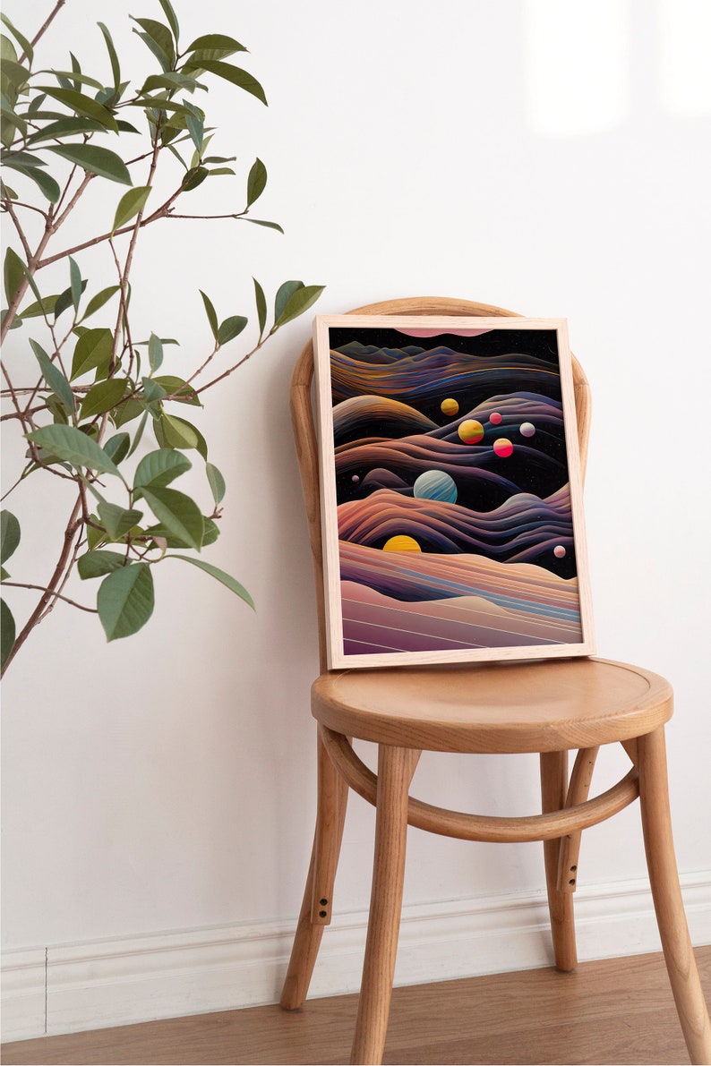 May include: A framed abstract art print with a dark background and colourful planets and stars. The print is in a light wood frame and is sitting on a wooden chair.
