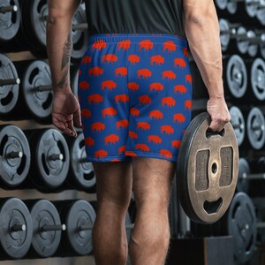 K&ouml;nnte beinhalten: Blaue Sporthose mit einem sich wiederholenden Muster aus orangefarbenen Bisons. Die Shorts haben einen elastischen Bund und sind aus leichtem, atmungsaktivem Stoff. Geeignet f&uuml;r Workouts oder Freizeitkleidung.