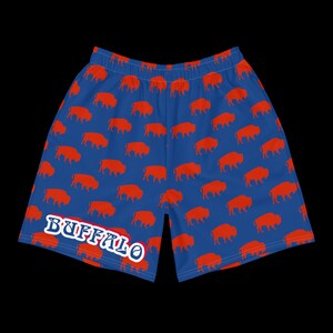 K&ouml;nnte beinhalten: Blaue Sporthose mit einem sich wiederholenden Muster aus orangefarbenen B&uuml;ffelsilhouetten. Das Wort "BUFFALO" ist wei&szlig; mit blauem Umriss auf dem linken Bein aufgedruckt. Die Shorts haben einen elastischen Bund.