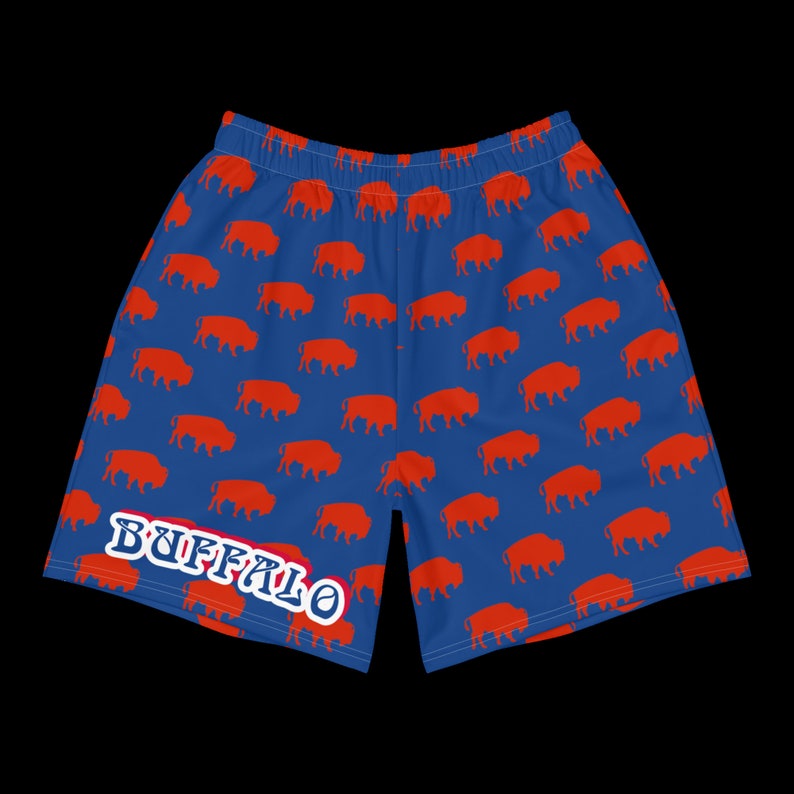 K&ouml;nnte beinhalten: Blaue Sporthose mit einem sich wiederholenden Muster aus orangefarbenen B&uuml;ffelsilhouetten. Das Wort "BUFFALO" ist wei&szlig; mit blauem Umriss auf dem linken Bein aufgedruckt. Die Shorts haben einen elastischen Bund.