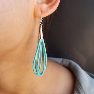 May include: Turquoise beaded earrings with silver-tone metal accents. The earrings feature a teardrop design with multiple strands of turquoise beads, accented with small yellow details. The top portion is a silver cone shape with a silver hook.