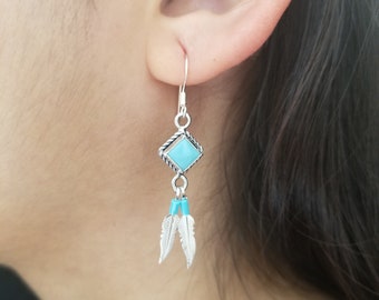 May include: Silver dangle earrings with a turquoise stone and two silver feathers.