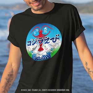 Puede incluir: Camiseta negra con un gráfico circular que presenta texto japonés y una criatura roja con forma de camarón. El diseño está sobre un fondo azul y verde con olas blancas. La camiseta tiene mangas cortas.