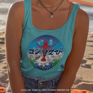 Puede incluir: Camiseta sin mangas turquesa con un diseño gráfico redondo que presenta una criatura roja similar a una langosta y texto japonés. El diseño está sobre un patrón de olas azules y blancas. La camiseta sin mangas se usa en la playa.