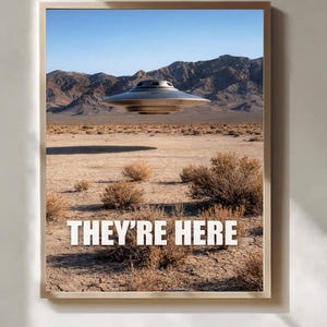 May include: A framed wall art print featuring a metallic, disc-shaped UFO hovering above a dry, arid desert landscape with sparse brown shrubs and distant mountains under a clear blue sky. The white text "THEY'RE HERE" is centered at the bottom.