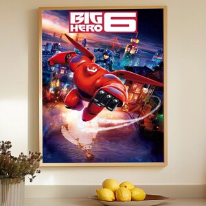 May include: A framed poster featuring the "Big Hero 6" movie. The artwork depicts a red robot in flight over a cityscape, with a character riding on its back. The title "BIG HERO 6" is displayed at the top in white and red.