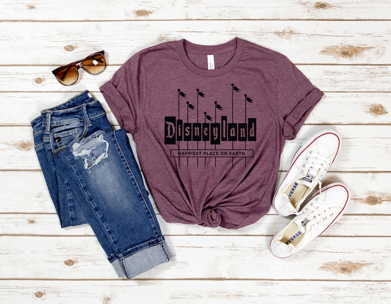 K&ouml;nnte beinhalten: Ein maroonfarbenes T-Shirt mit einer schwarzen Grafik des Disneyland-Logos und dem Text "Happiest Place on Earth".