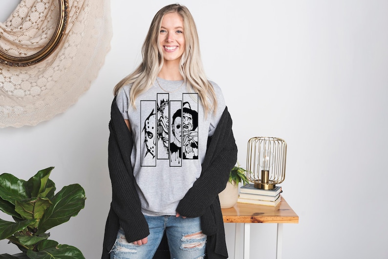 May include: A gray t-shirt with a black and white graphic of four horror movie characters. The characters are in black and white and are wearing masks. The graphic is in a square shape and is centered on the shirt.