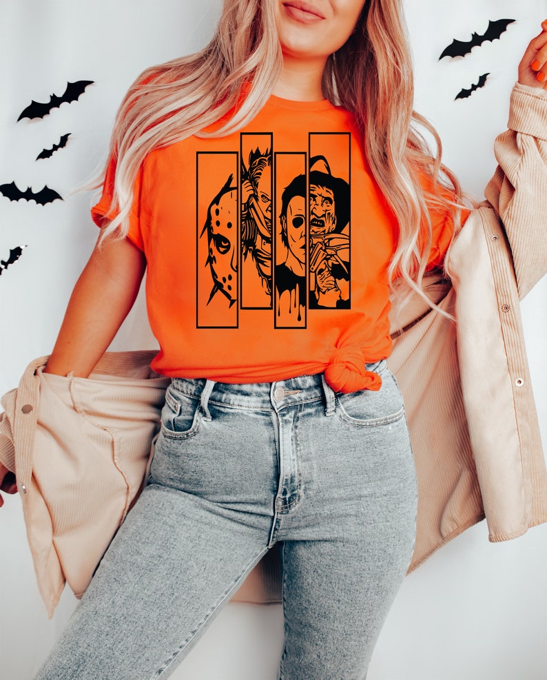 May include: A bright orange t-shirt with a black graphic of four horror movie characters. The characters are in black and white and are arranged in a row. The graphic includes Jason Voorhees, Michael Myers, Freddy Krueger, and Leatherface.