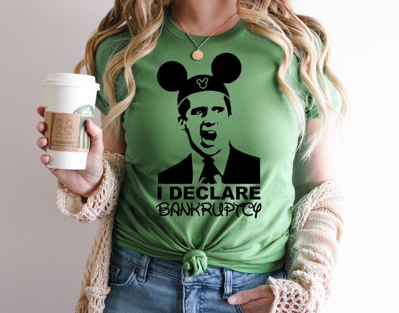 May include: A green t-shirt with a black and white image of a man wearing a Mickey Mouse hat. The text "I DECLARE BANKRUPTCY" is printed below the image.