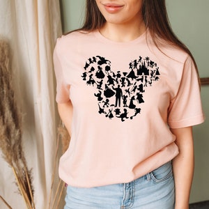 May include: A pink t-shirt featuring a black silhouette of Mickey Mouse's head formed from various Disney characters.