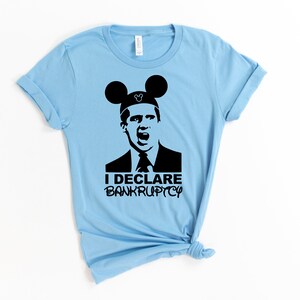 May include: A light blue t-shirt with a black silhouette of a man wearing Mickey Mouse ears. The man is shouting and the text "I DECLARE BANKRUPTCY" is below him.