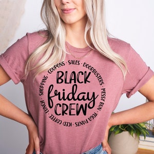 May include: A pink t-shirt with a black circle graphic that says "Black Friday Crew" with the words "Shopping, Coupons, Sales, Doorbusters, Messy Bun, Yoga Pants, Iced Coffee, Lunch" around the circle.