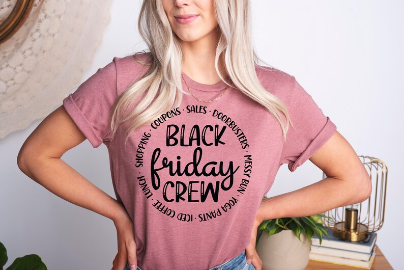May include: A pink t-shirt with a black circle graphic that says "Black Friday Crew" with the words "Shopping, Coupons, Sales, Doorbusters, Messy Bun, Yoga Pants, Iced Coffee, Lunch" around the circle.