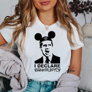 May include: A white t-shirt with a black and white image of a man wearing Mickey Mouse ears. The man is making a surprised expression and the text "I DECLARE BANKRUPTCY" is printed below the image.