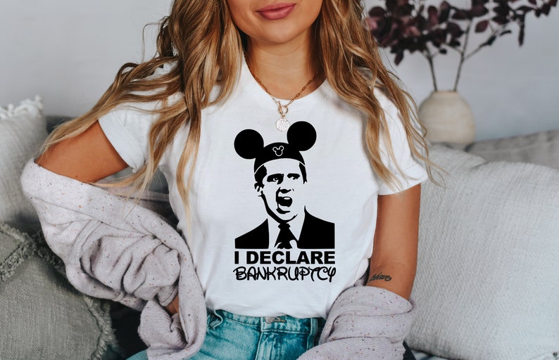 May include: A white t-shirt with a black and white image of a man wearing Mickey Mouse ears. The man is making a surprised expression and the text "I DECLARE BANKRUPTCY" is printed below the image.