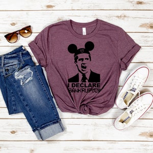 May include: A maroon t-shirt with a black silhouette of a man wearing Mickey Mouse ears and the text "I Declare Bankruptcy".