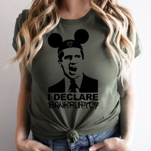 May include: A green t-shirt with a black and white image of a character from the TV show "The Office" wearing Mickey Mouse ears. The text "I DECLARE BANKRUPTCY" is printed below the image.