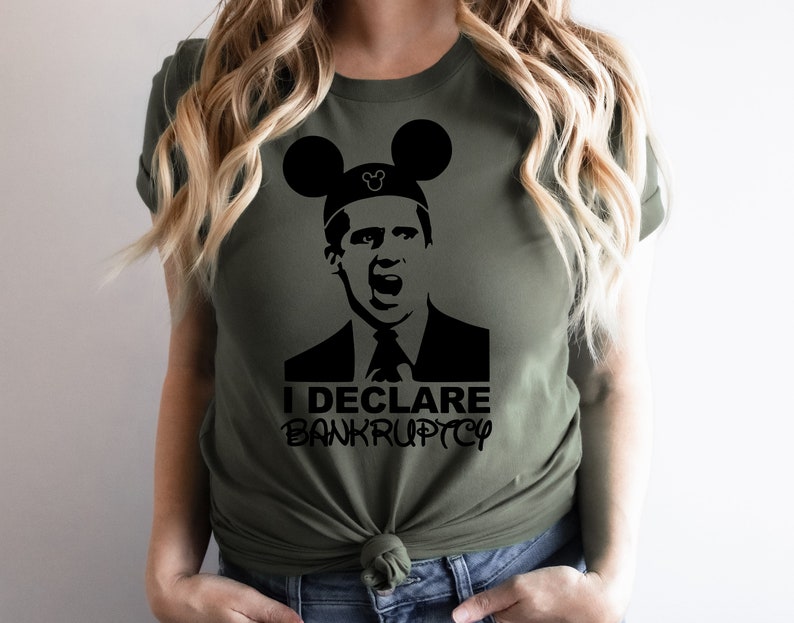 May include: A green t-shirt with a black and white image of a character from the TV show "The Office" wearing Mickey Mouse ears. The text "I DECLARE BANKRUPTCY" is printed below the image.