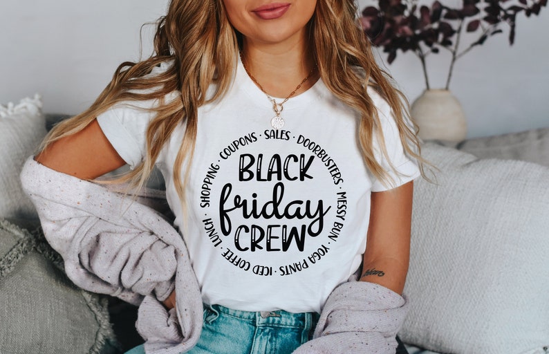 May include: White t-shirt with a black circle graphic that says "Black Friday Crew" with text around the circle that says "Yoga Pants, Iced Coffee, Lunch, Shopping, Coupons, Sales, Doorbusters, Messy Bun".