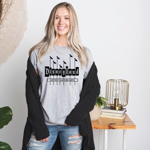 K&ouml;nnte beinhalten: Ein graues T-Shirt mit einer schwarzen Grafik des Disneyland-Schilds und dem Text "Happiest Place on Earth".
