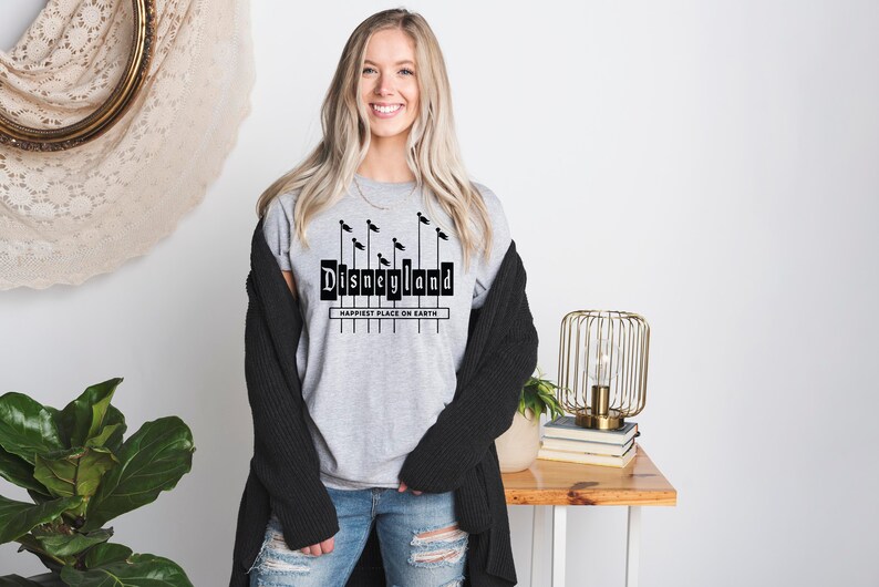 K&ouml;nnte beinhalten: Ein graues T-Shirt mit einer schwarzen Grafik des Disneyland-Schilds und dem Text "Happiest Place on Earth".