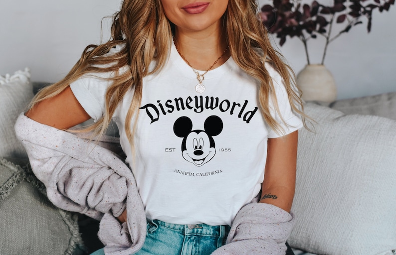 K&ouml;nnte beinhalten: Wei&szlig;es T-Shirt mit einem schwarzen Mickey Mouse-Motiv und dem Text "Disneyworld Est. 1955 Anaheim, Kalifornien".