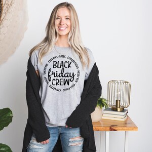 May include: A gray t-shirt with a black circle graphic that says "Black Friday Crew" surrounded by the words "Shopping, Coupons, Sales, Doorbusters, Messy Bun, Red Pants, Iced Coffee, Late Night,  Free Prints".