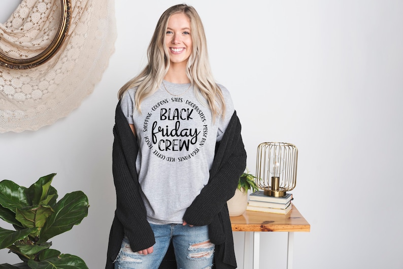 May include: A gray t-shirt with a black circle graphic that says "Black Friday Crew" surrounded by the words "Shopping, Coupons, Sales, Doorbusters, Messy Bun, Red Pants, Iced Coffee, Late Night,  Free Prints".