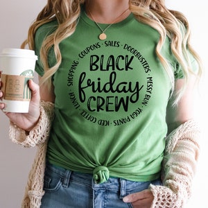 May include: A green t-shirt with a black circle graphic that says "Black Friday Crew" with a list of activities around the circle, including "iced coffee", "yoga pants", "messy bun", and "doorbusters".