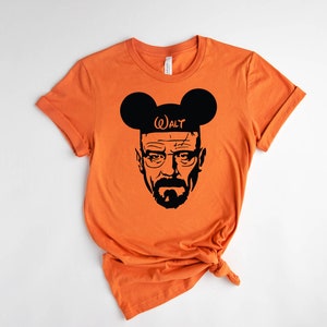 May include: Orange t-shirt with a black silhouette of Walter White from Breaking Bad wearing Mickey Mouse ears with the text "(W)ALT" on the headband.
