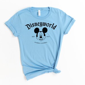 K&ouml;nnte beinhalten: Hellblaues T-Shirt mit einem schwarzen Mickey Mouse Kopf und dem Text "Disneyworld Est. 1955 Anaheim, Kalifornien".