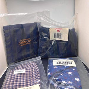 Könnte beinhalten: Eine Auswahl an Longaberger-Produkten in Kunststoffverpackungen. Zu den Artikeln gehören ein marineblau gestreifter Artikel, ein blau-weiß karierter Artikel und ein blauer Artikel mit weißen Sternen und roten Akzenten. Die Verpackung enthält das Longaberger-Logo und Produktinformationen.