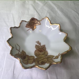 Peut inclure: Un plat en porcelaine blanche avec un bord festonné et une bordure dorée. Le plat est décoré d'un motif floral de roses et de feuilles en or.